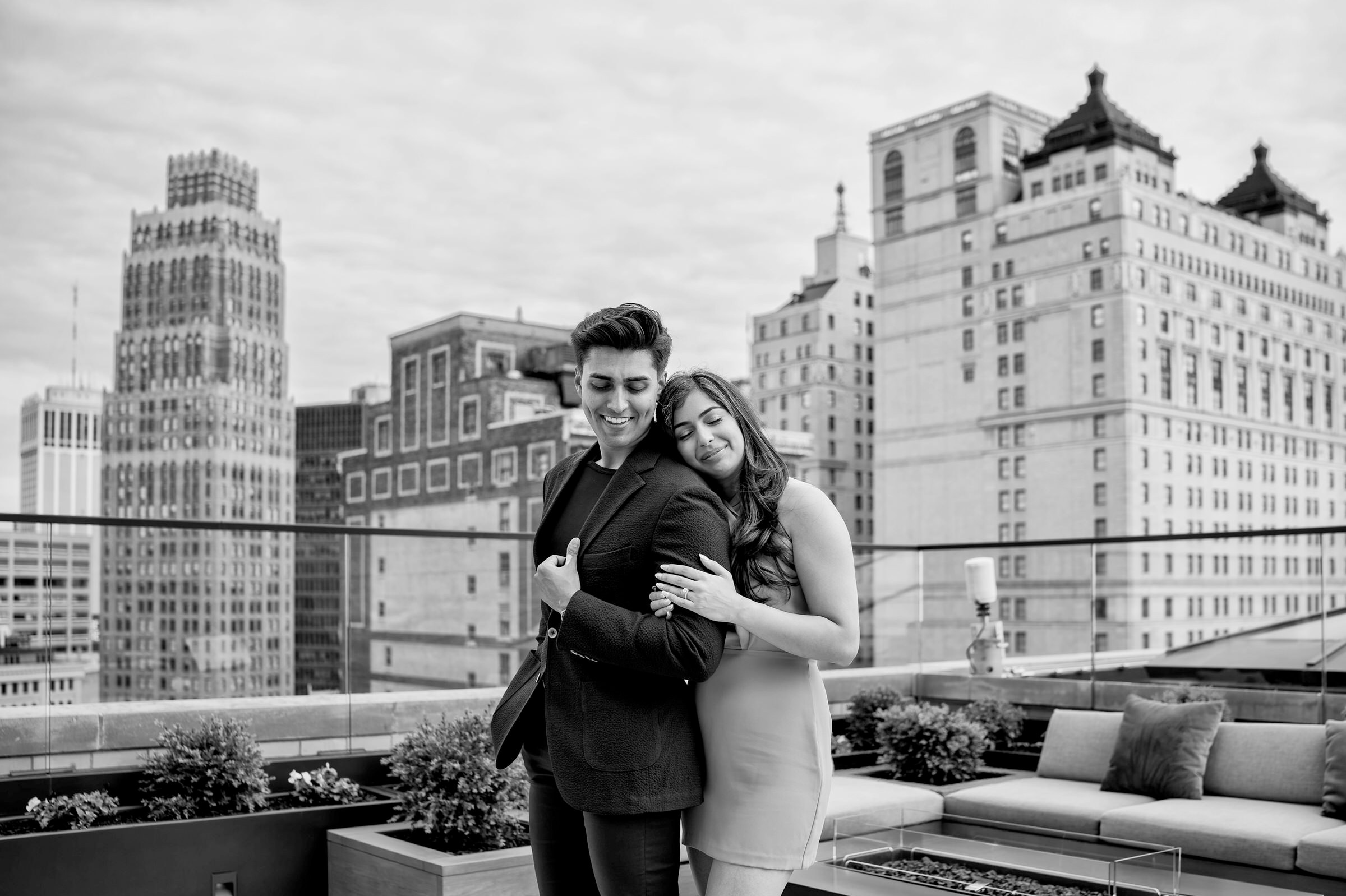 A fiancé hugs her fiancee from behind following their Kamper's rooftop proposal at the Book Tower in Detroit. 