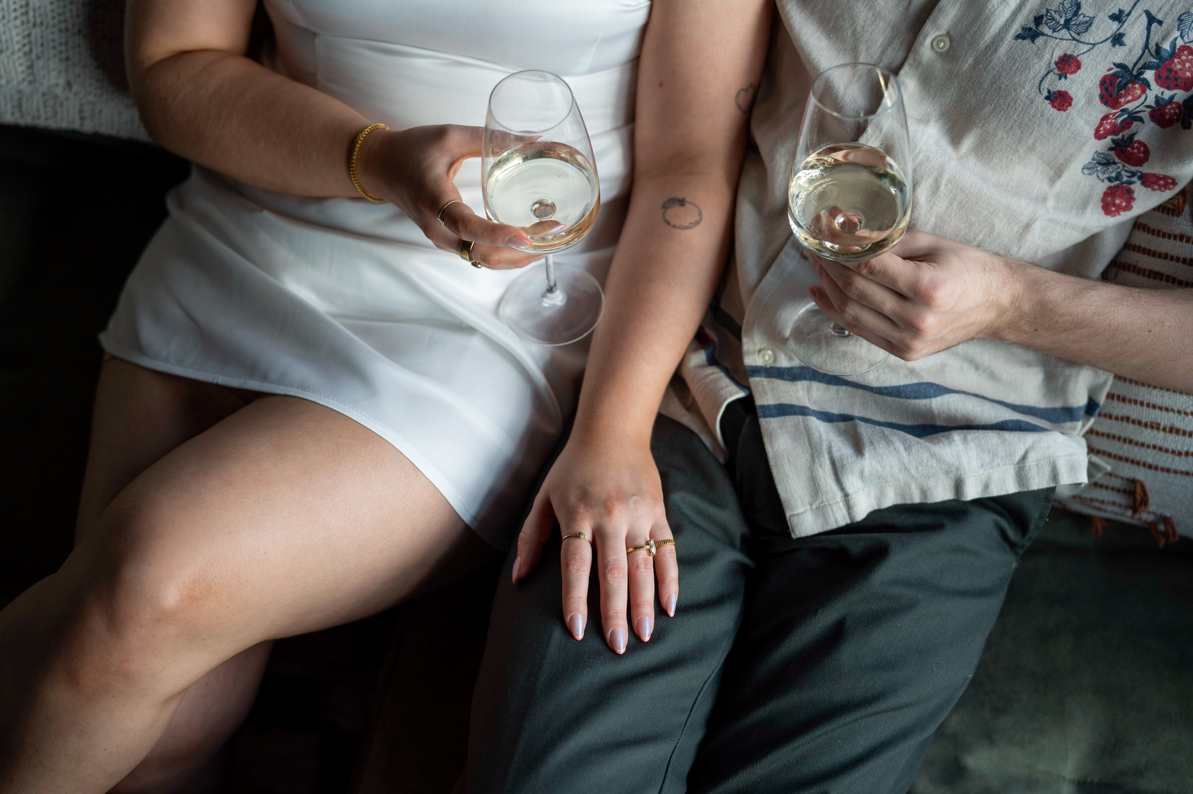 A close up of hands and wine glasses on a couch. 