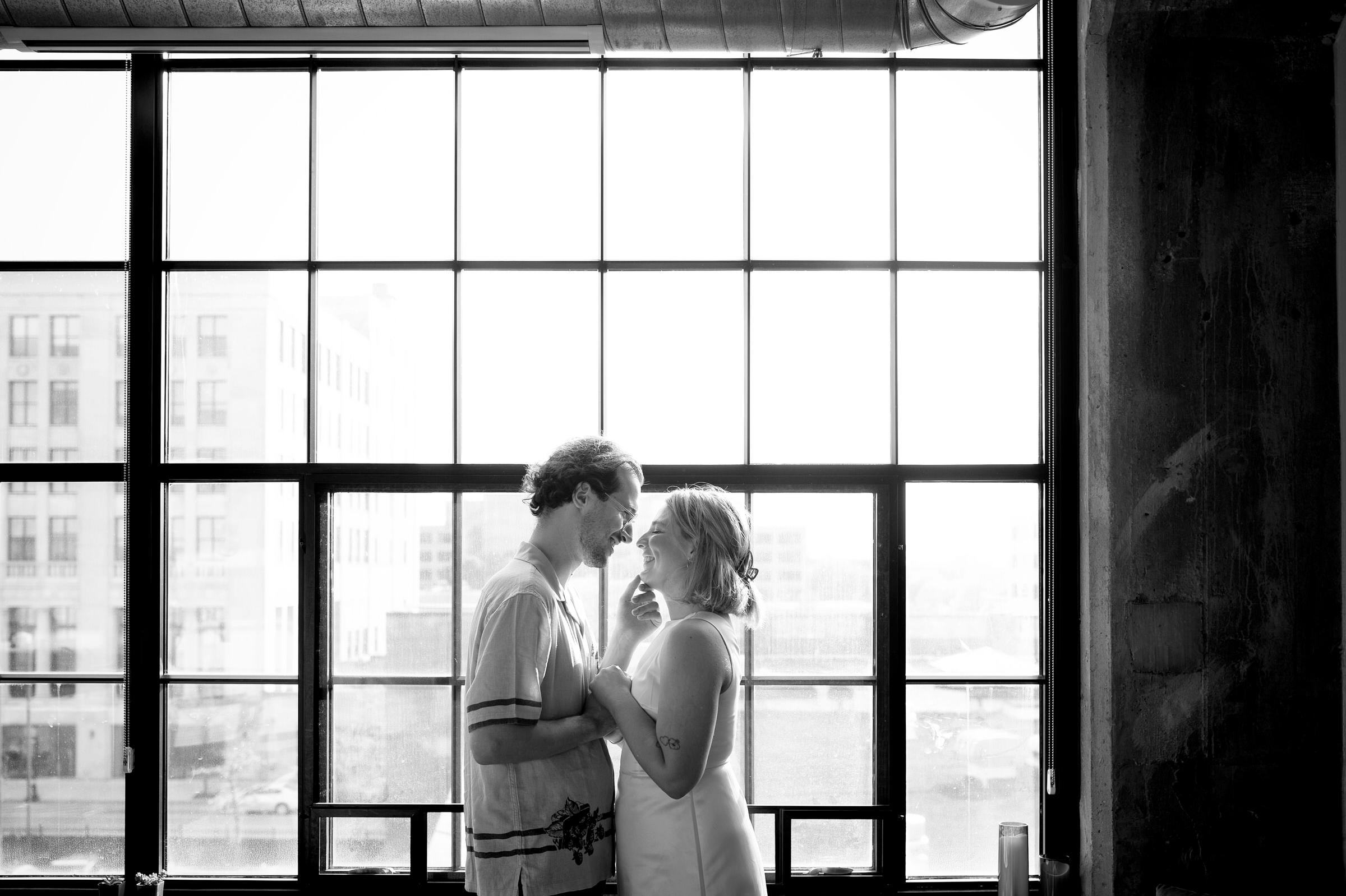 Standing in front of a window, a couple almost kisses during their Detroit lifestyle engagement session.  