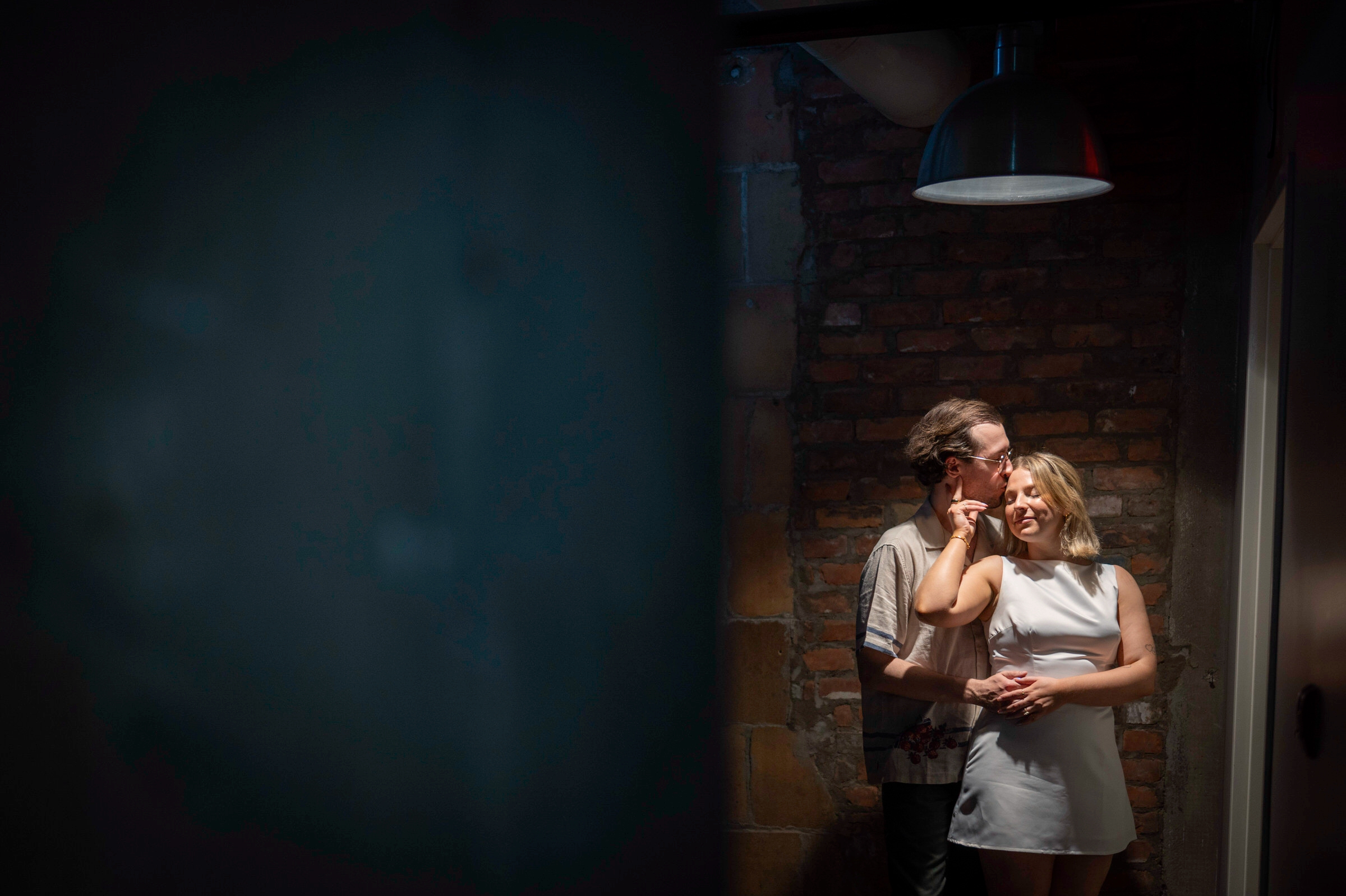 Illuminated by an overhead light, a gentleman kisses the forehead of his fiance during their Detroit lifestyle engagement session.  