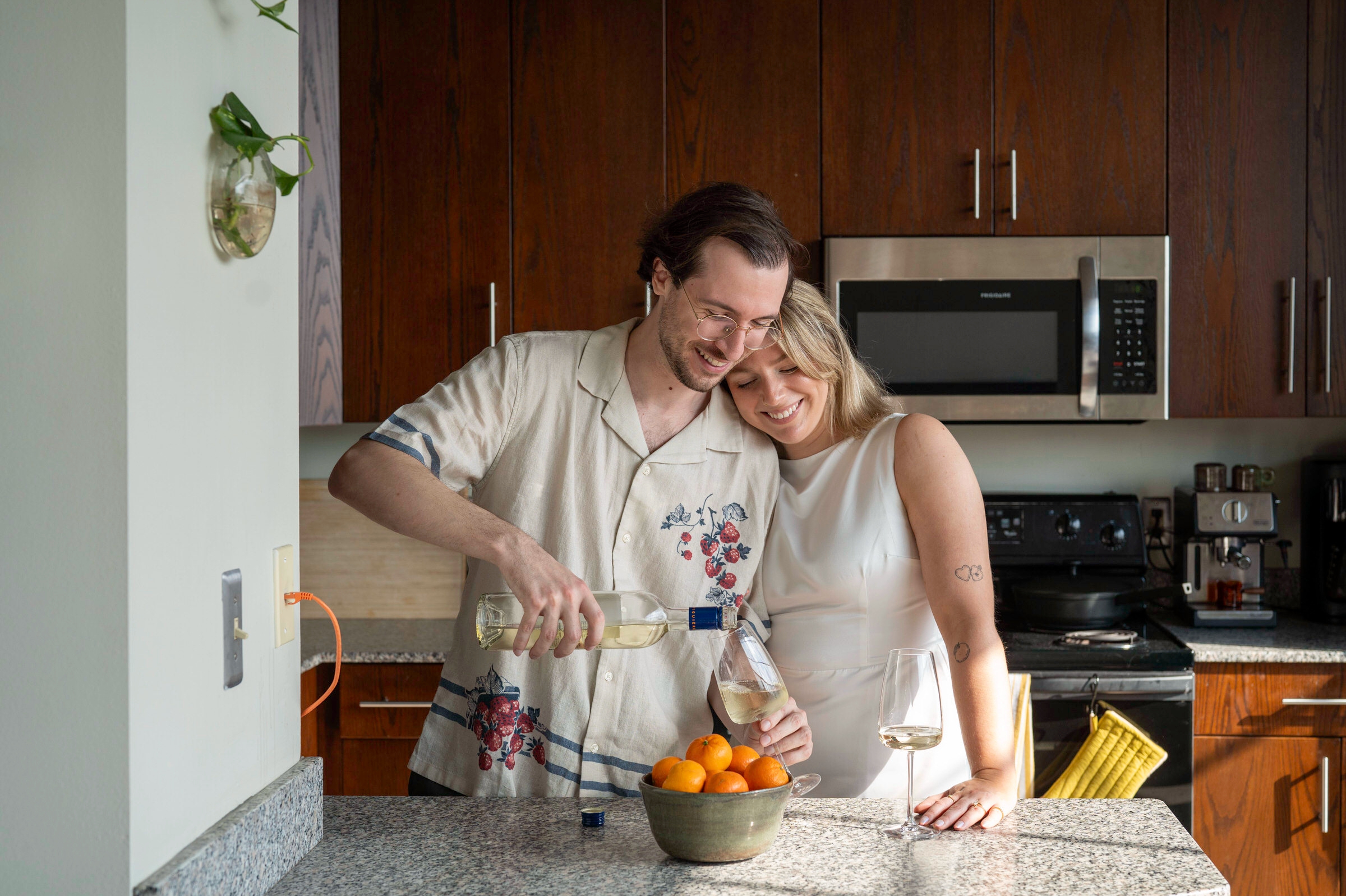 A couple pours a glass of wine in their kitchen during their lifestyle engagement session. 