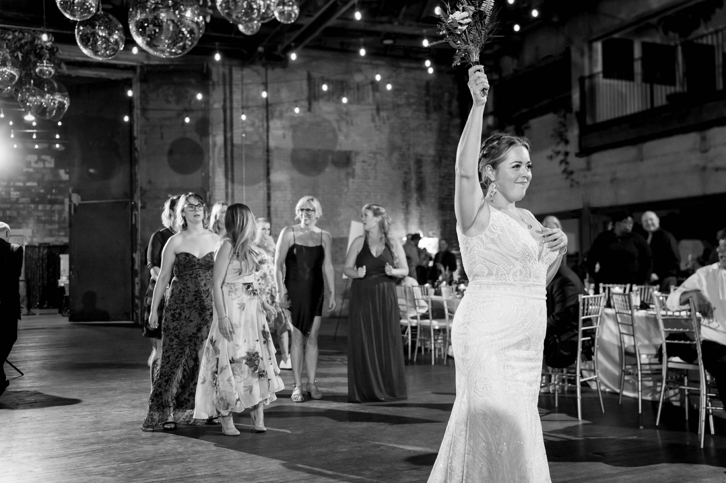 A bride holds a bouquet above her head before the bouquet toss at her Jam Handy wedding.  