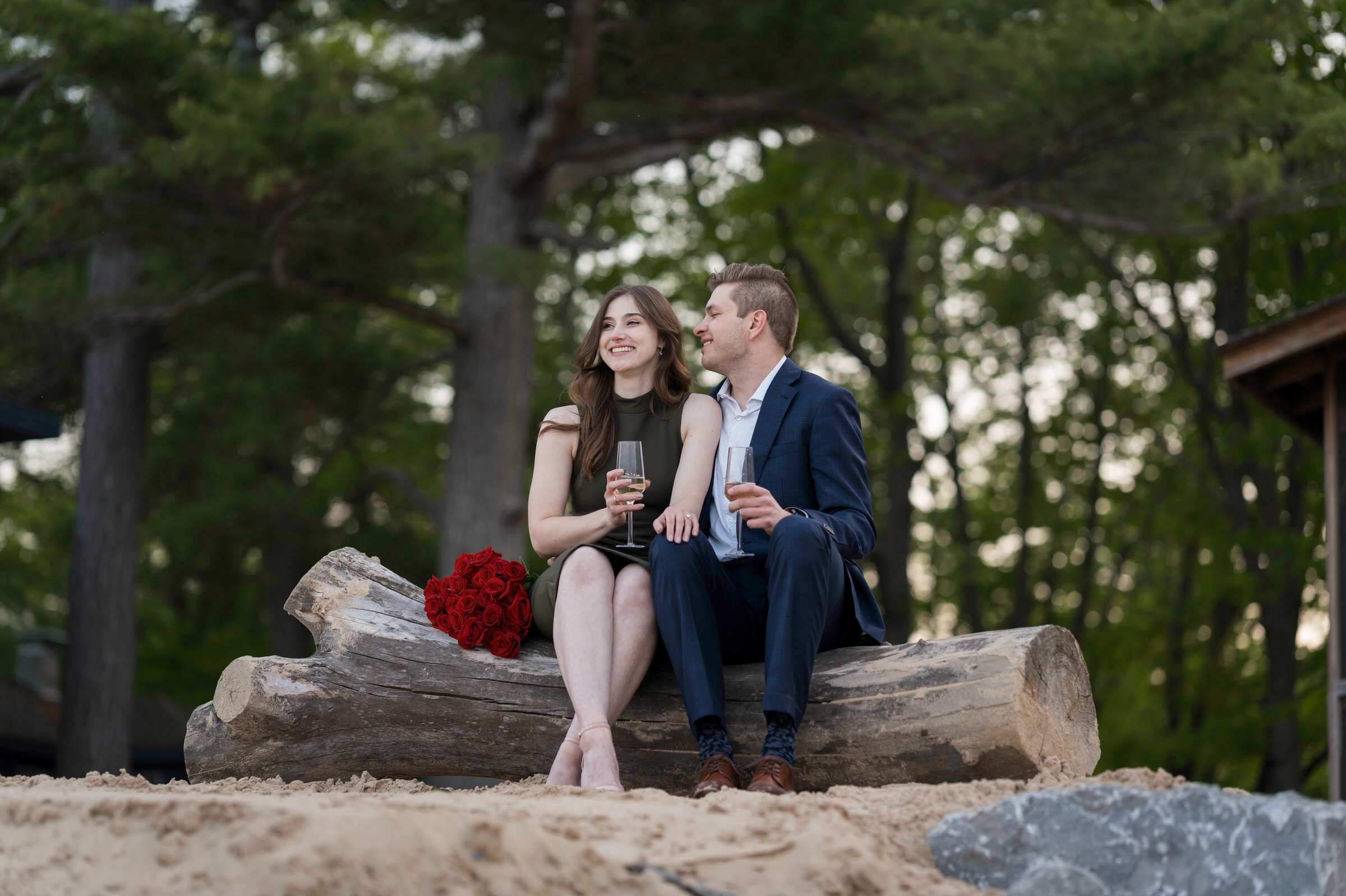 Couple laughs with champagne glasses after proposal on the Shores of Oscoda